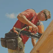 A man using a nail gun on a wooden roof during construction.