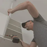 Image of a man wearing a grey shirt while assembling a white cabinet.