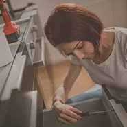 A woman repairing a drawer in a kitchen.